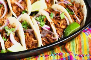 5 mole pork tacos topped with thinly sliced red onion, bright green cilantro and lime wedges on a dark black plate