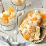 Five Cup Salad being scooped from a large white bowl with a wooden spoon and served into small clear glass trifle dishes