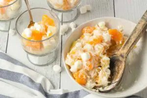 Five Cup Salad being scooped from a large white bowl with a wooden spoon and served into small clear glass trifle dishes