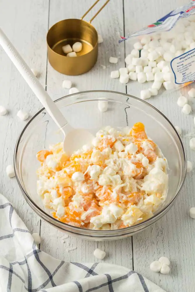 Five Cup Salad mixed and prepared in a large glass mixing bowl with mini marshmallows scattered around