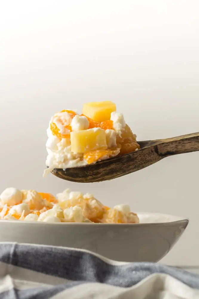 Five Cup Salad being scooped from a large white bowl with a wooden spoon