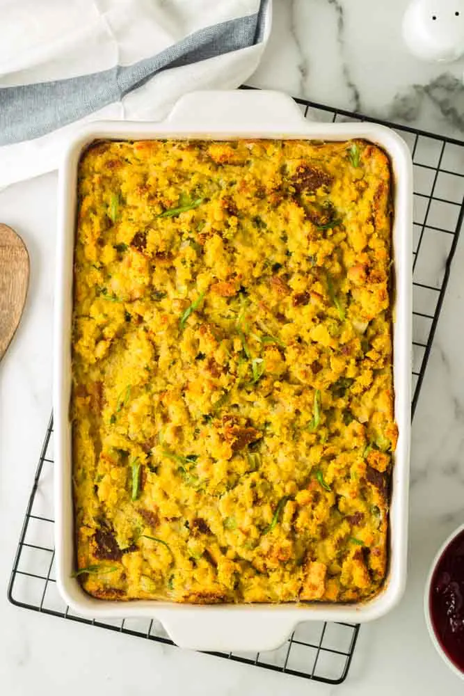 large white casserole dish filled with prepared traditional southern cornbread dressing sitting on a black cooling rack