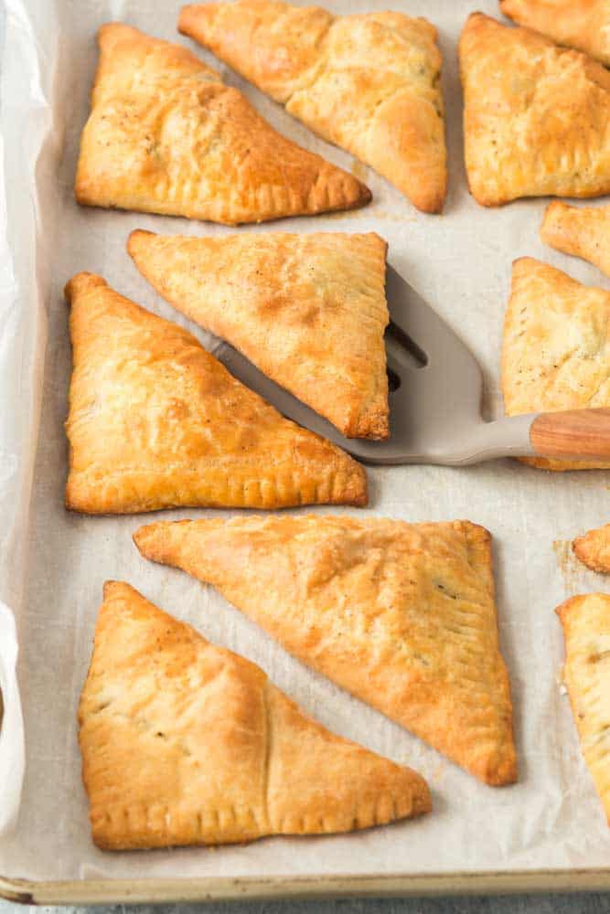 Louisiana Meat Pies on a parchment lined baking sheet with a spatula lifting one pie from the pan