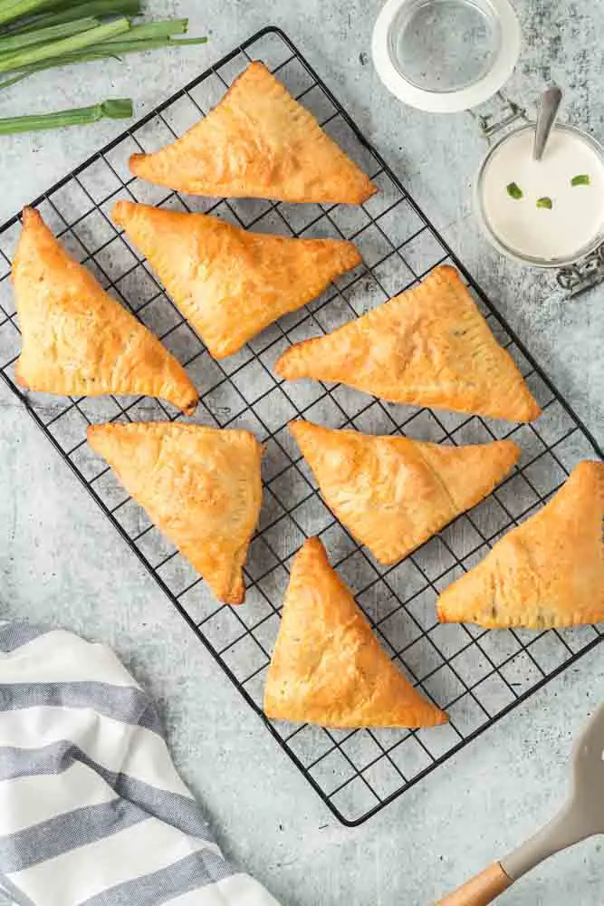 Louisiana Meat Pies on a black cooling rack with side of horseradish cream sauce