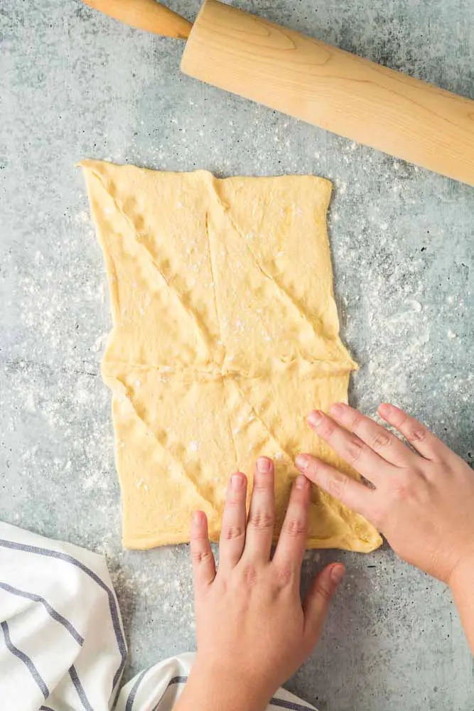 crescent dough on a grey concrete surface showing hands pinch the seams of the dough together to make one piece of dough