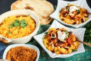 two star shaped dishes filled with orange rice and red chicken curry topped with green cilantro and white dollop of yogurt and a beige bowl filled with orange rice