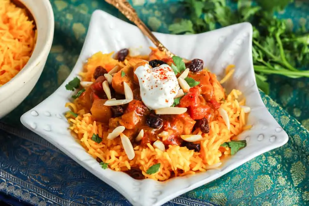 star shaped dish filled with orange rice topped with red chicken curry and a white dollop of yogurt