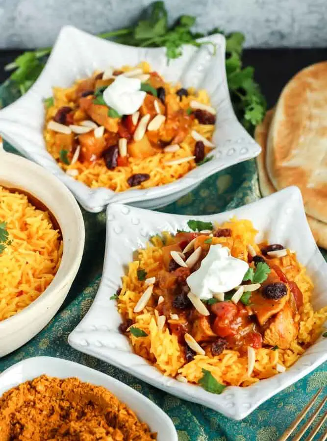 two star shaped dishes filled with orange rice and red chicken curry topped with green cilantro and white dollop of yogurt