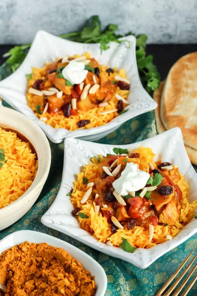 two star shaped dishes filled with orange rice and red chicken curry topped with green cilantro and white dollop of yogurt