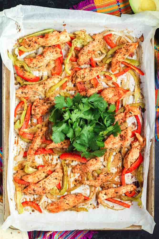 Sheet pan fajitas on a gold baking sheet lined with parchment paper topped with bright green cilantro