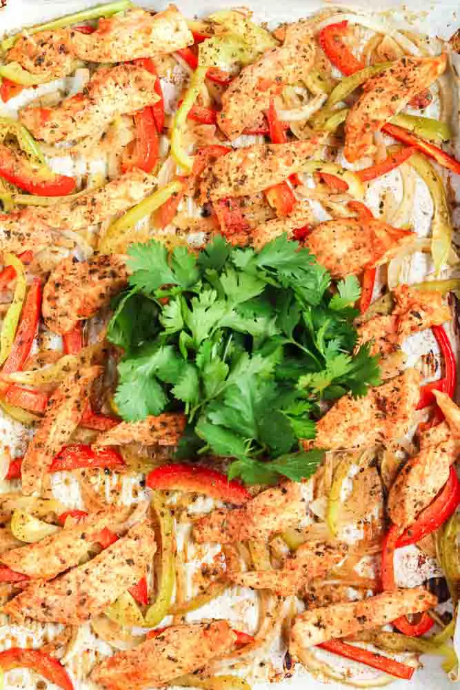 Sheet pan fajitas on a gold baking sheet lined with parchment paper topped with bright green cilantro