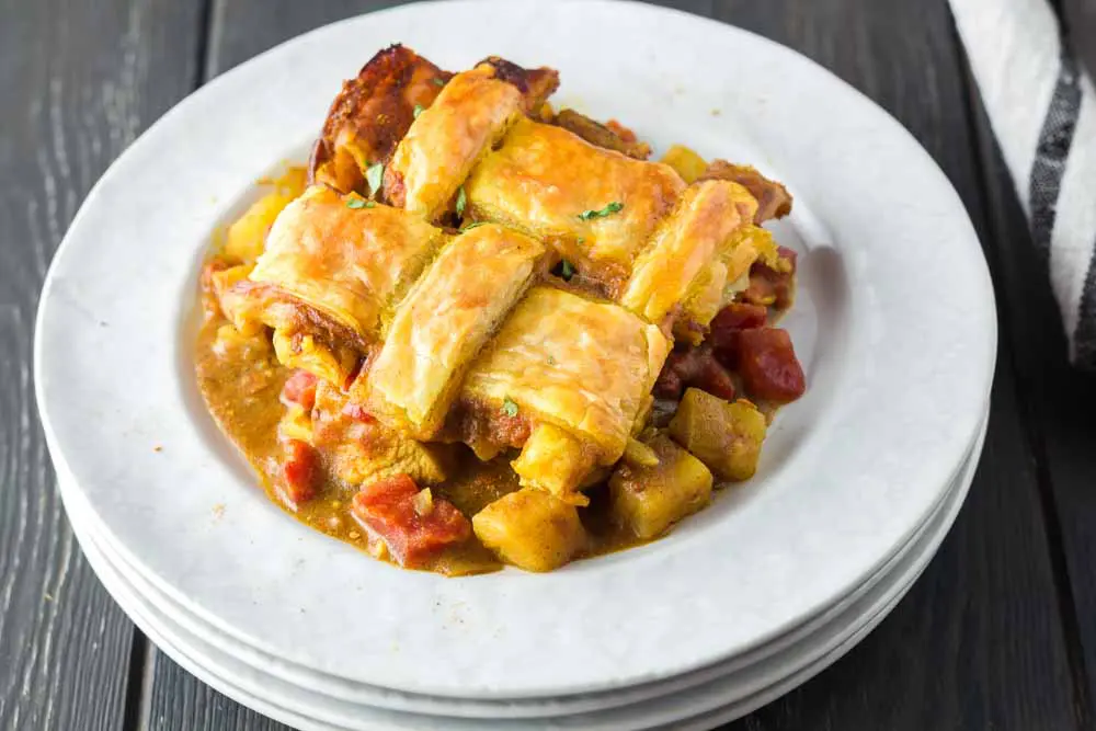 Chicken curry pot pie dished out onto a white plate featuring a golden brown lattice puff pastry topping