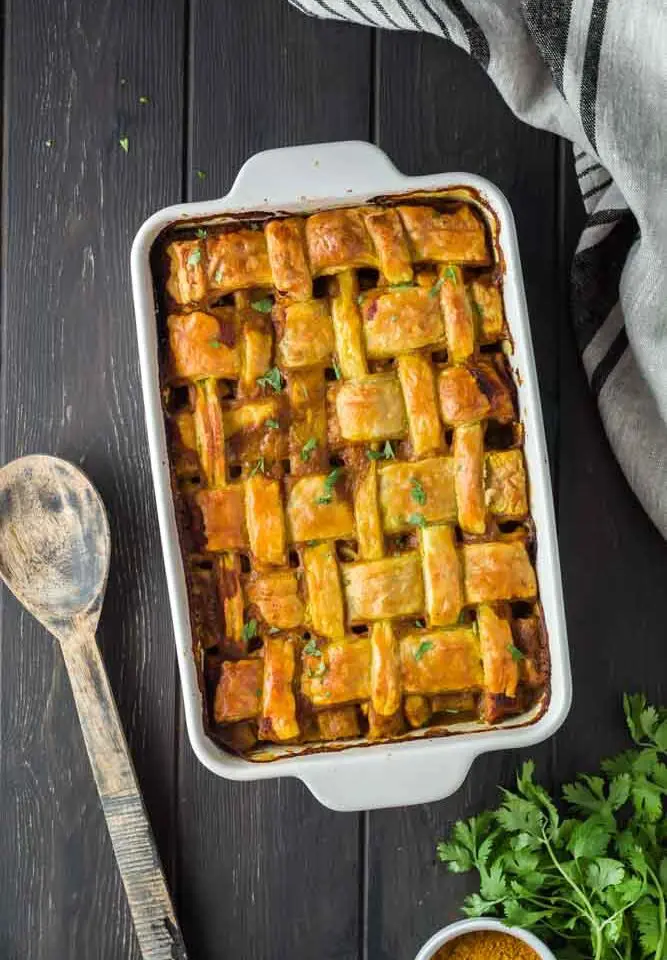 Chicken curry pot pie in a white baking dish featuring a golden brown lattice puff pastry topping