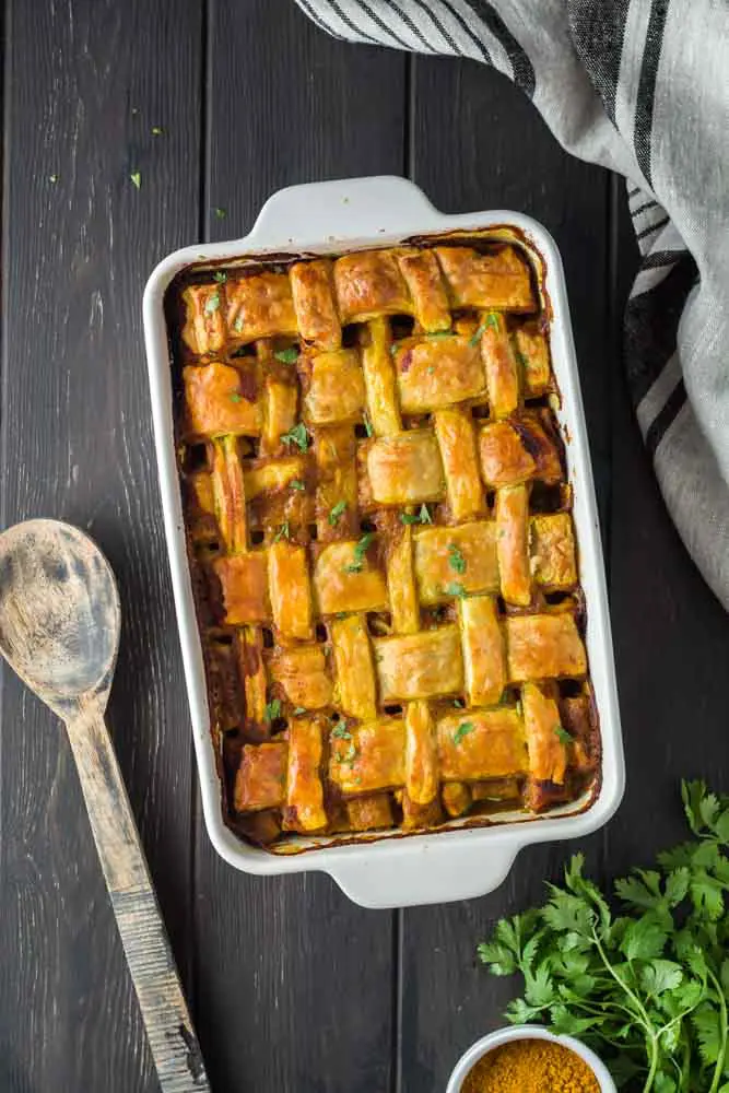 Chicken curry pot pie in a white baking dish featuring a golden brown lattice puff pastry topping