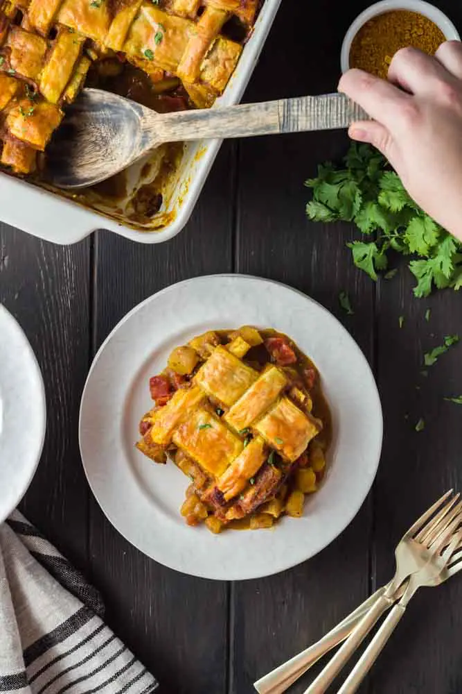 Chicken curry pot pie dished out onto a white plate featuring a golden brown lattice puff pastry topping