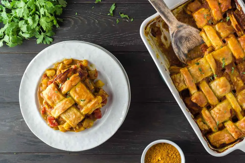 Chicken curry pot pie dished out onto a white plate featuring a golden brown lattice puff pastry topping