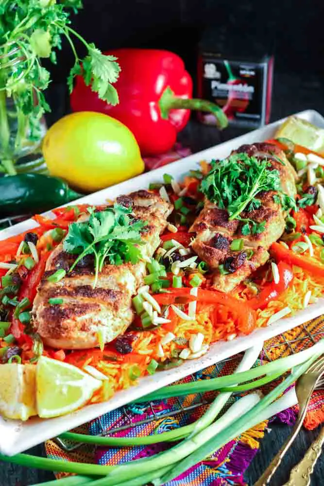 white rectangular plate filled with orange rice topped with strips of red bell pepper, green onion pieces, sliced chicken breast and cilantro with a lemon wedge