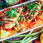 white rectangular plate filled with orange rice topped with strips of red bell pepper, green onion pieces, sliced chicken breast and cilantro with a lemon wedge