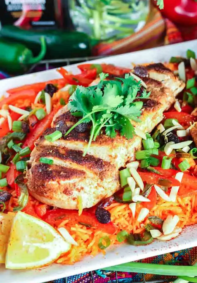 white rectangular plate filled with orange rice topped with strips of red bell pepper, green onion pieces, sliced chicken breast and cilantro with a lemon wedge