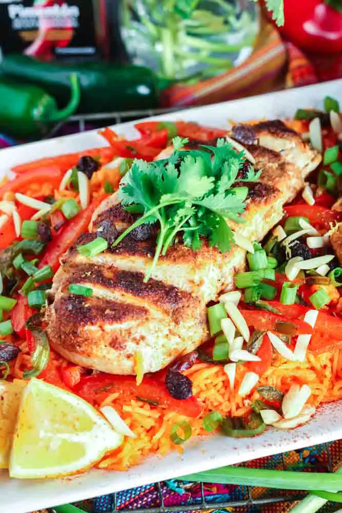 white rectangular plate filled with orange rice topped with strips of red bell pepper, green onion pieces, sliced chicken breast and cilantro with a lemon wedge