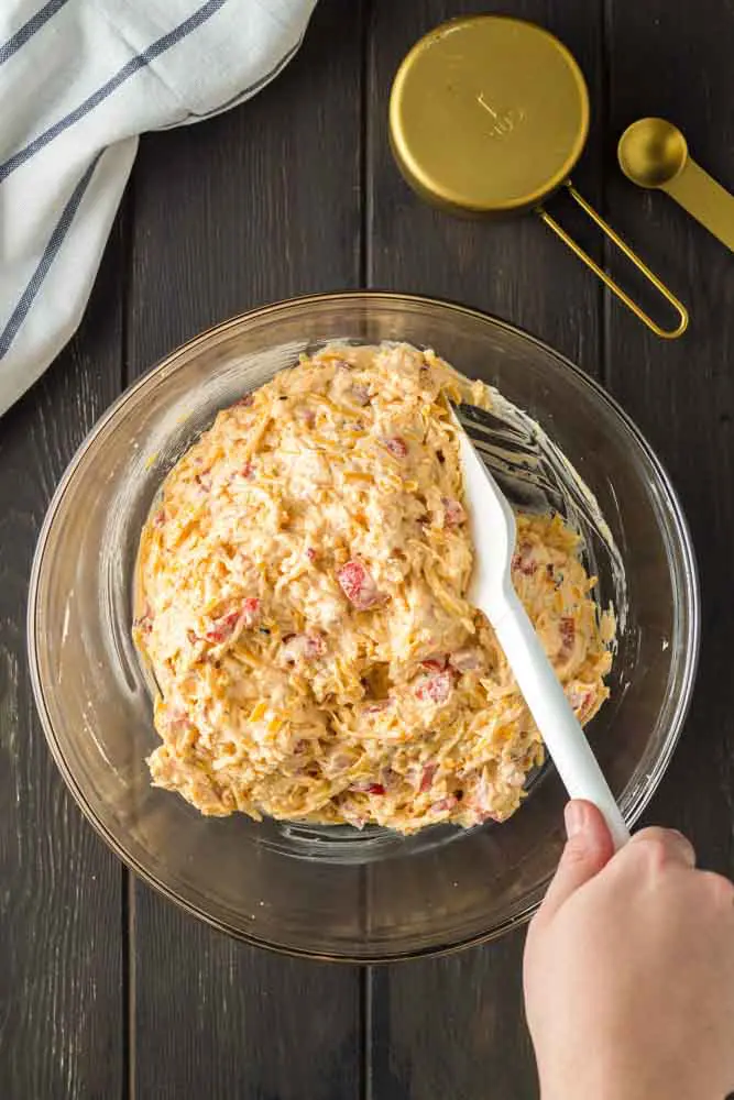 clear glass bowl filled with prepared pimento cheese being stirred with a white spatula