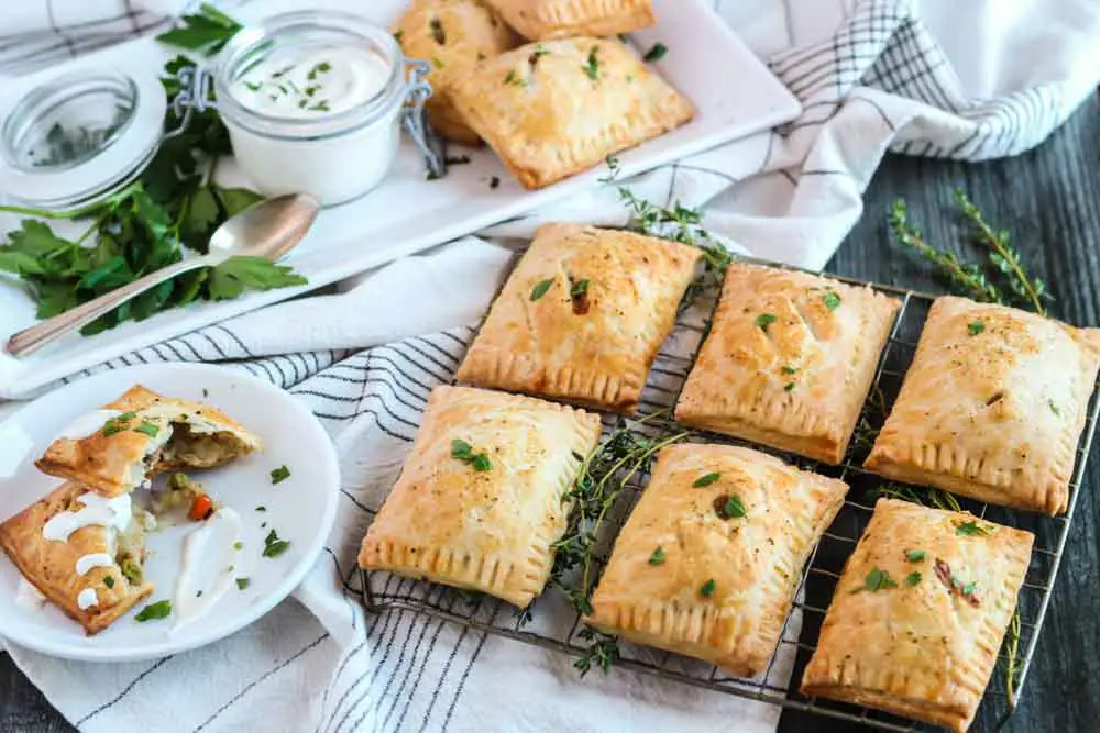 two rows of three shepherd's hand pies on a cooling rack with one pie split open on a small white plate