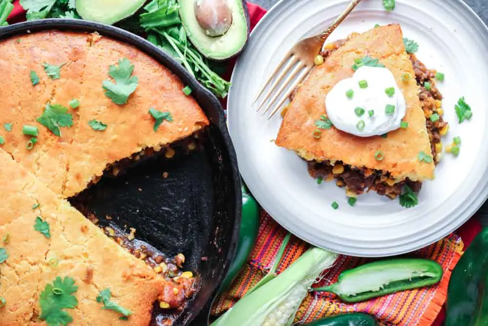 A sour cream topped wedge of cornbread over a mixture of meat and vegetables