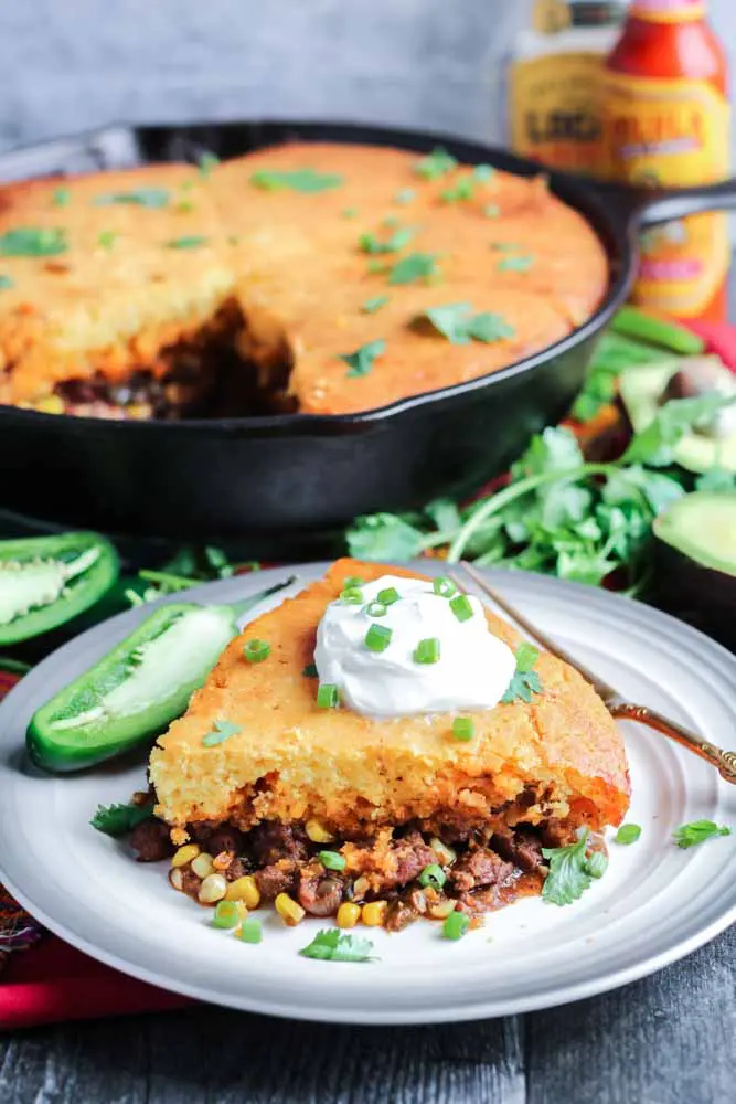 a portion of taco cornbread pie garnished with sour cream and sliced green onions on a round plate