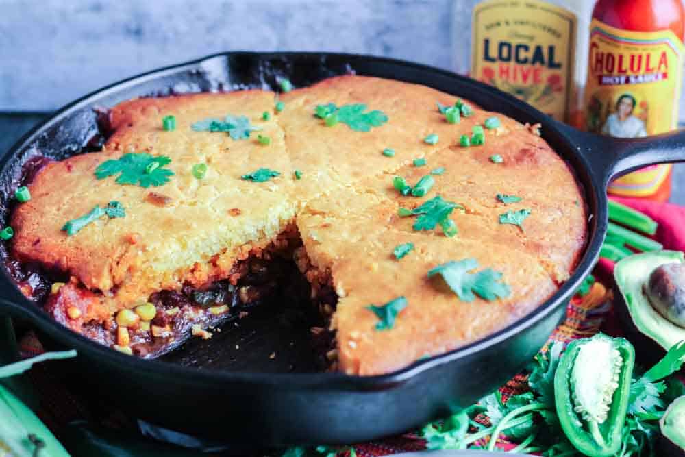 cornbread over meat and corn in a cast iron skillet