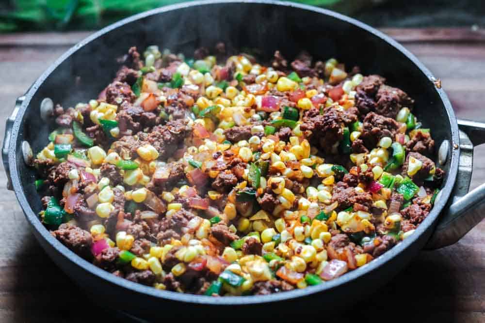 a mixture of corn, meat, diced green pepper and diced red onion in a black skillet