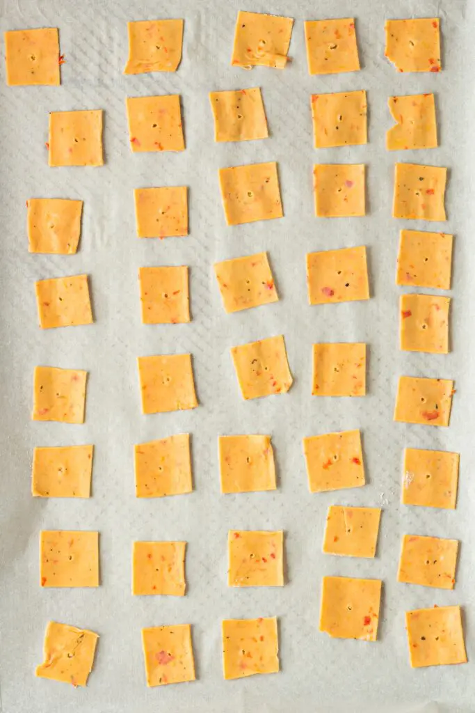 Uncooked bright orange dough cut into squares and laid on white parchment paper