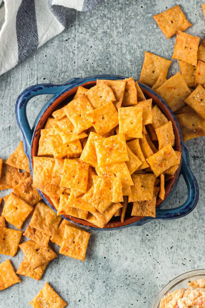 Bright orange square crackers with a single hole in the middle spilling out of a bright blue bowl
