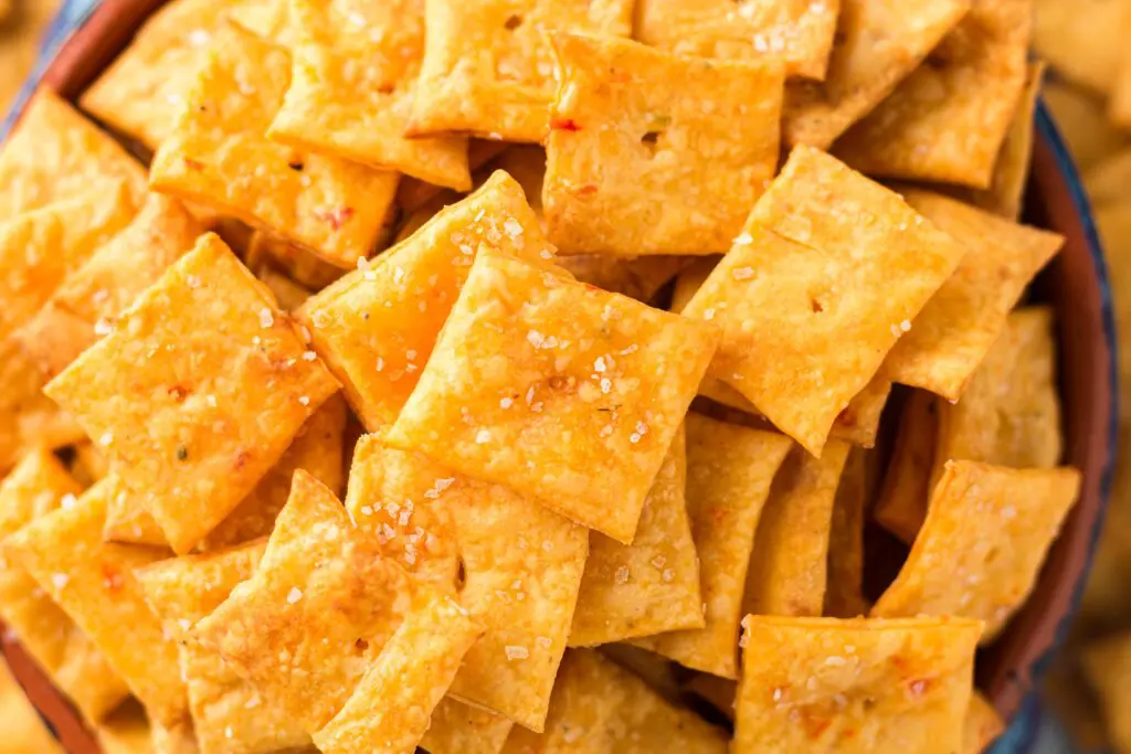 Bright orange square crackers with a single hole in the middle spilling out of a bright blue bowl