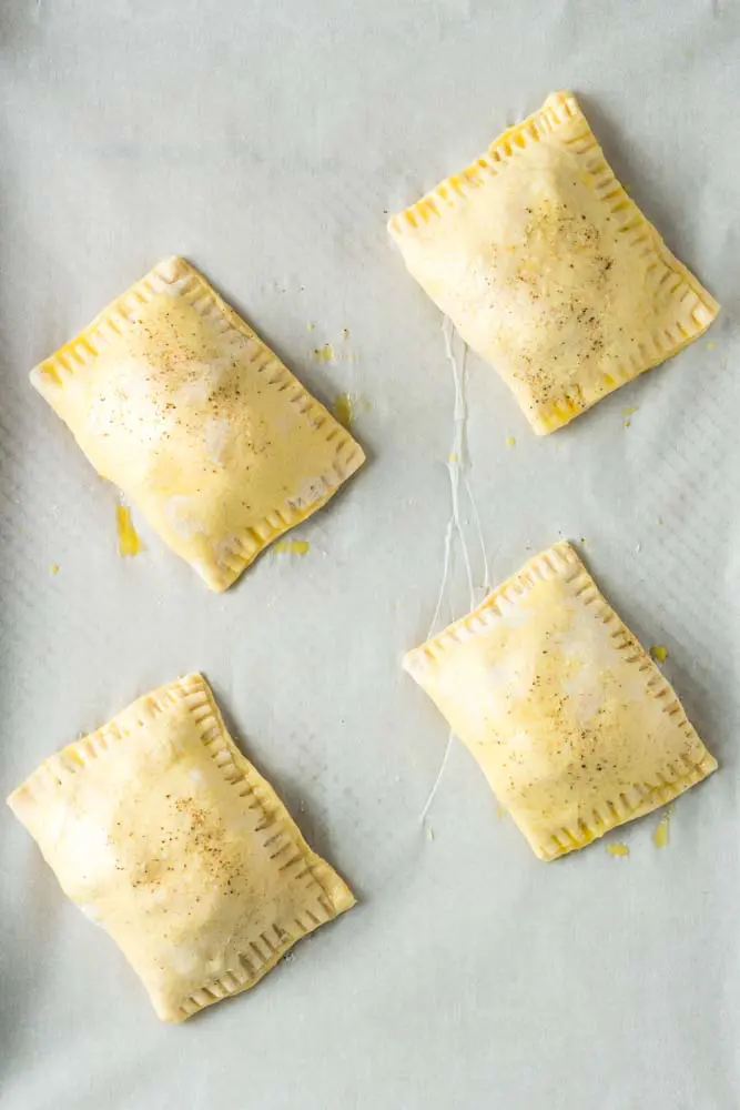 Four uncooked pimento cheeseburger hand pies sitting on a white piece of parchment paper