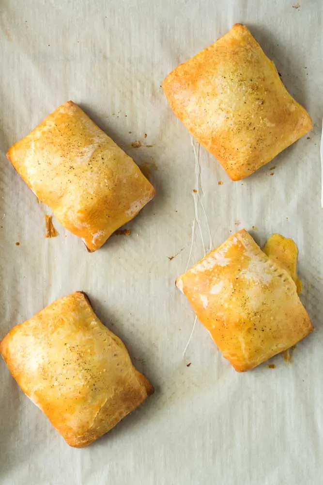 Four pimento cheeseburger hand pies fresh from the oven sitting on a white piece of parchment paper