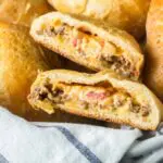 pimento cheeseburger hand pies in a basket lined with a blue and white towel with one split in two to show to gooey pimento cheese filling inside