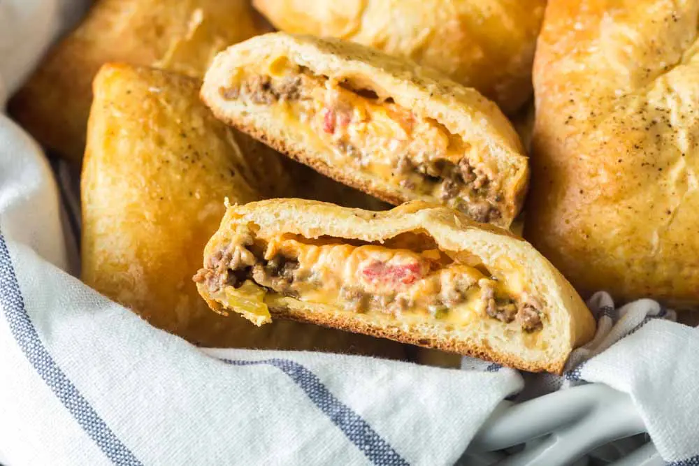 pimento cheeseburger hand pies in a basket lined with a blue and white towel with one split in two to show to gooey pimento cheese filling inside