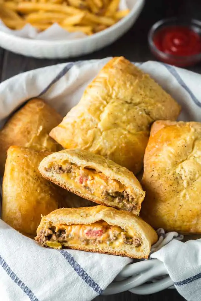 pimento cheeseburger hand pies in a basket lined with a blue and white towel with one split in two to show to gooey pimento cheese filling inside