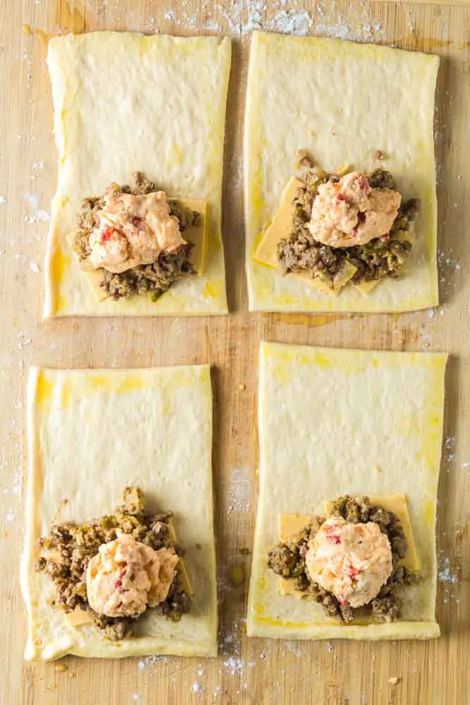 four uncooked pimento cheeseburger hand pies before sealing the edges sitting on a wooden cutting board