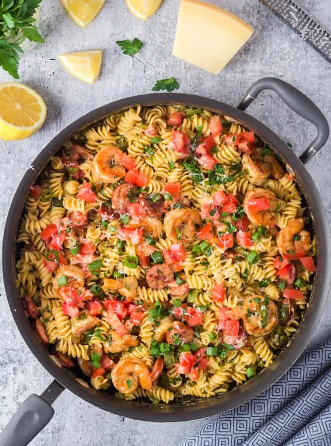 Large black saute pan filled with Cajun Shrimp Pasta with rotini pasta, andouille sausage rounds, bright red tomatoes and bell peppers and sliced green onions