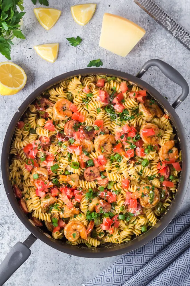 Large black saute pan filled with Cajun Shrimp Pasta with rotini pasta, andouille sausage rounds, bright red tomatoes and bell peppers and sliced green onions