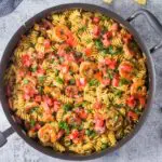 Large black saute pan filled with Cajun Shrimp Pasta with rotini pasta, andouille sausage rounds, bright red tomatoes and bell peppers and sliced green onions