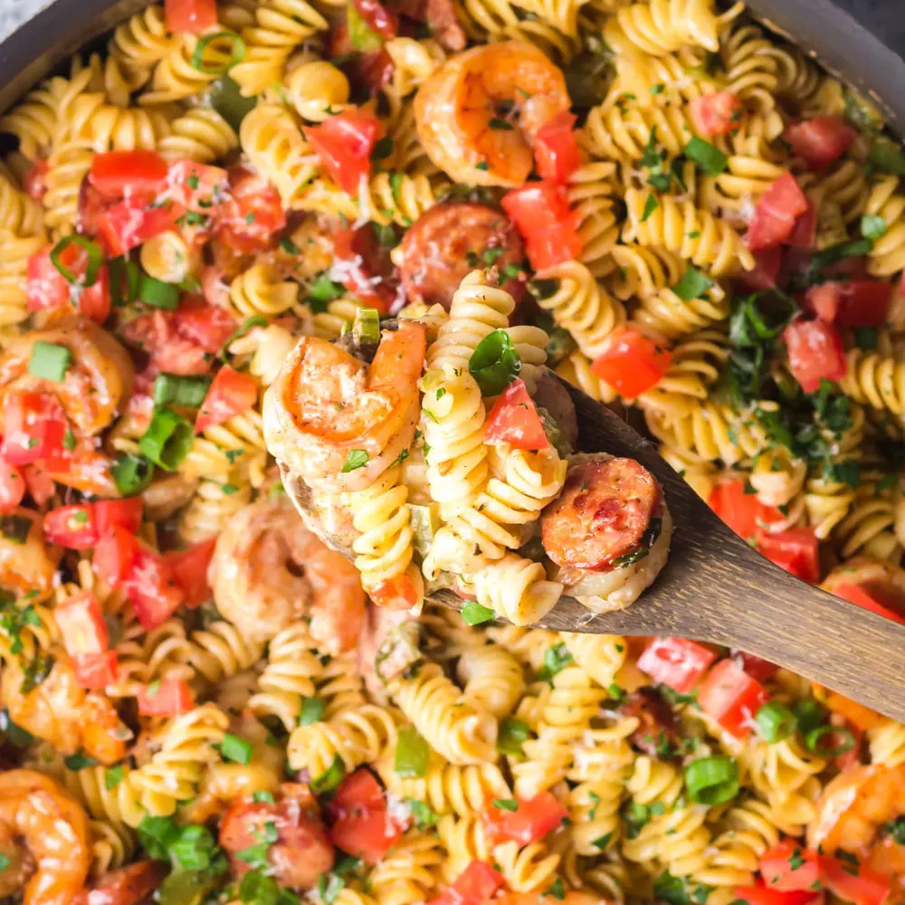 Background of Cajun Shrimp Pasta being scooped with a dark wooden spoon