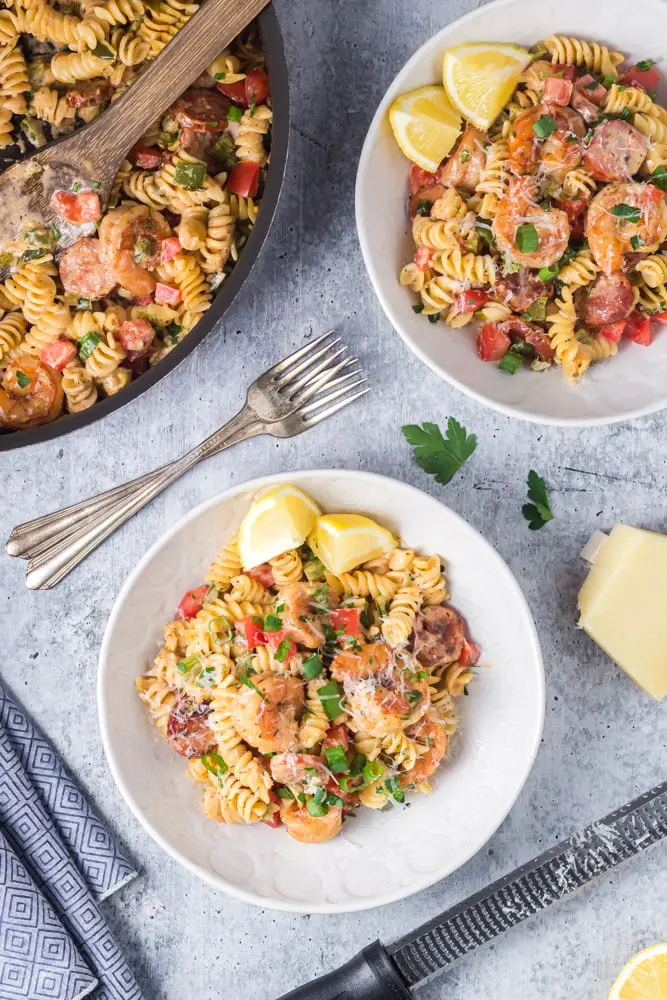 Two white bowls filled with Cajun Shrimp Pasta with rotini pasta, andouille sausage rounds, bright red tomatoes and bell peppers and sliced green onions