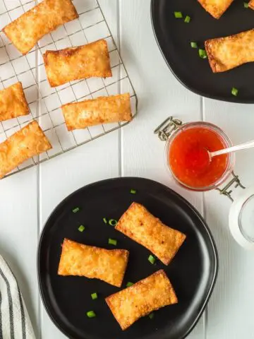 Golden brown rectangular pimento cheese wontons on small black plate and a cooling rack with a side of bright red thai sweet chili dipping sauce