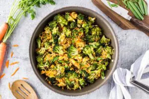 Saute pan filled with bright green broccoli florets, grated carrots, sliced green onions and fried rice