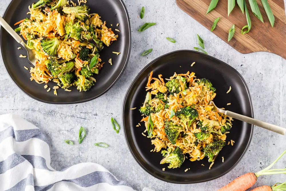 Two black plates filled with bright green broccoli florets, grated carrots, sliced green onions and fried rice