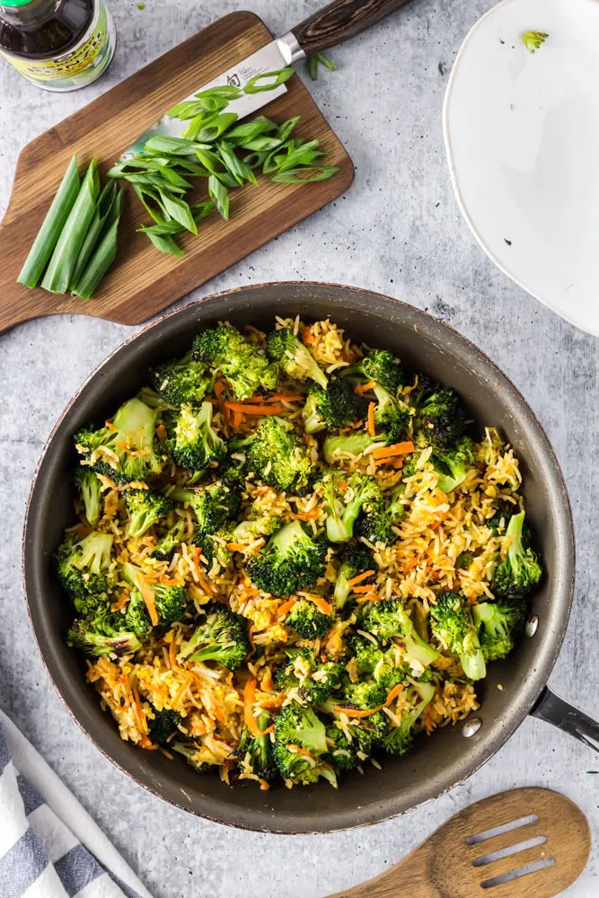 Saute pan filled with bright green broccoli florets, grated carrots, sliced green onions and fried rice