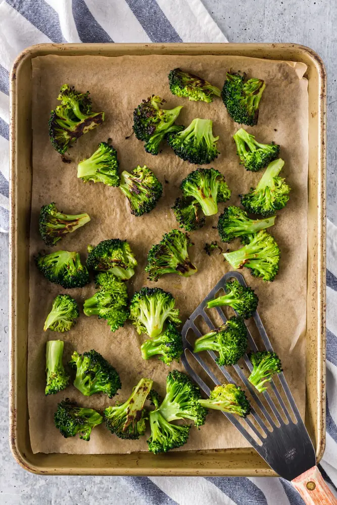 bright green roasted broccoli with charred edges on a parchment lined baking sheet after roasting in the oven