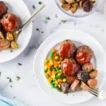 Two plates of Onion Burger Mini Meatloaf covered in a bright red sauce with carrots, pea, and green beans on the side